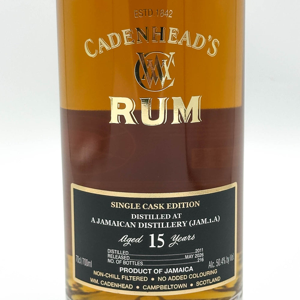 A close-up of a Cadenhead's Rum bottle showing the amber liquid, gold lettering, and a black label with white text.