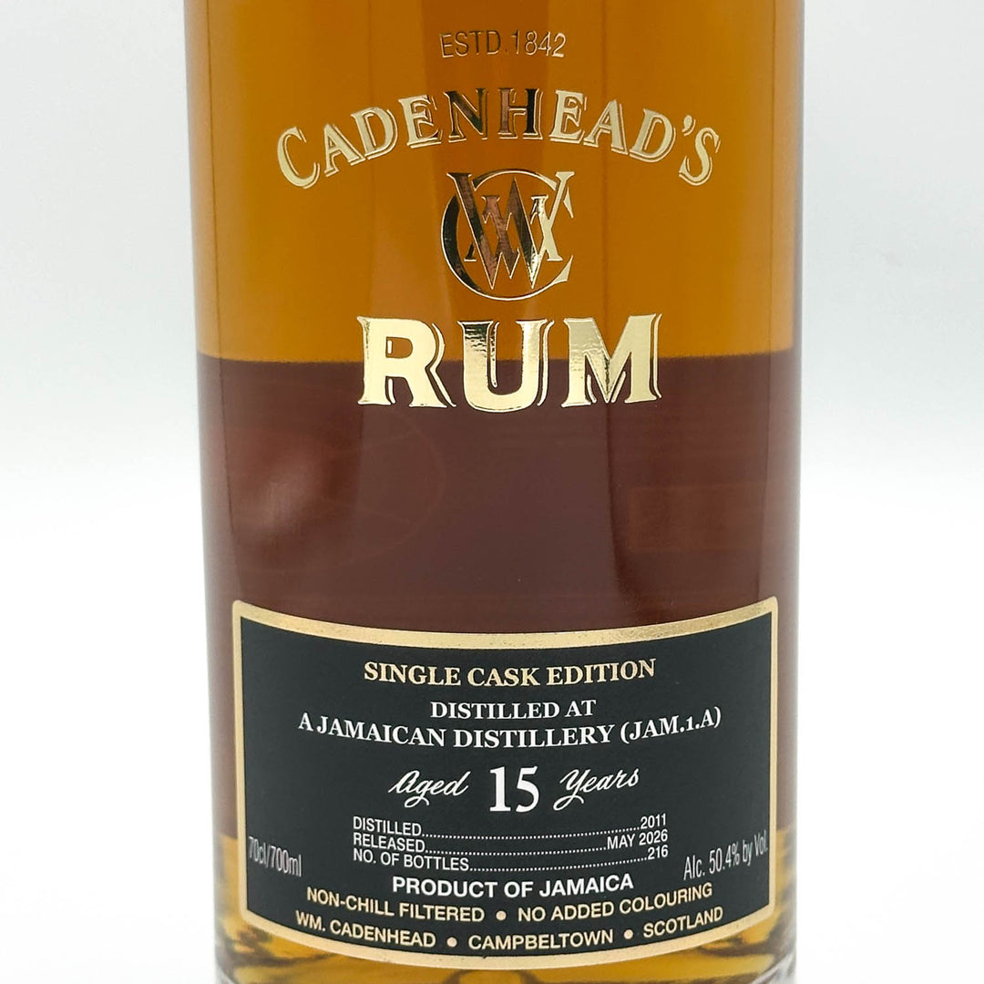 A close-up of a Cadenhead's Rum bottle showing the amber liquid, gold lettering, and a black label with white text.