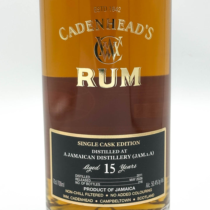 A close-up of a Cadenhead's Rum bottle showing the amber liquid, gold lettering, and a black label with white text.
