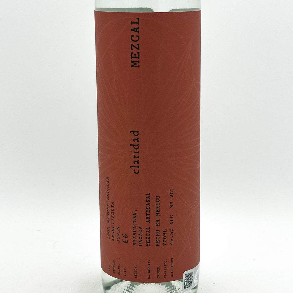 A clear glass bottle of Mezcal Claridad on a white background, showing a reddish-brown label with black text.