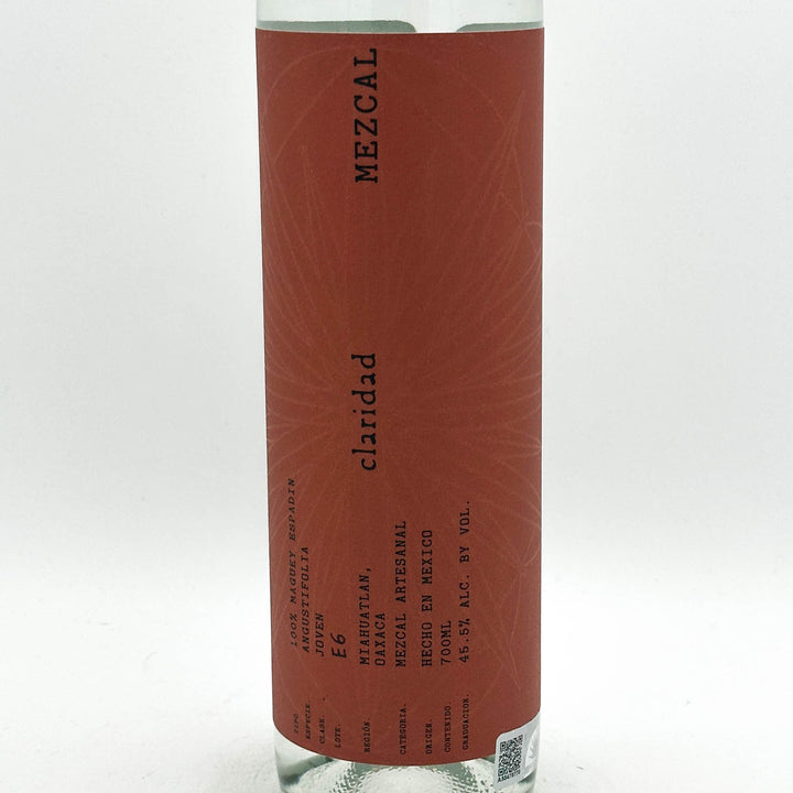 A clear glass bottle of Mezcal Claridad on a white background, showing a reddish-brown label with black text.