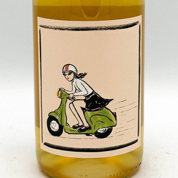 A close-up of a wine bottle showing a cream-colored label with a vintage-style illustration of a woman riding a green scooter. The bottle contains a pale golden-yellow liquid and is photographed against a plain white background.
