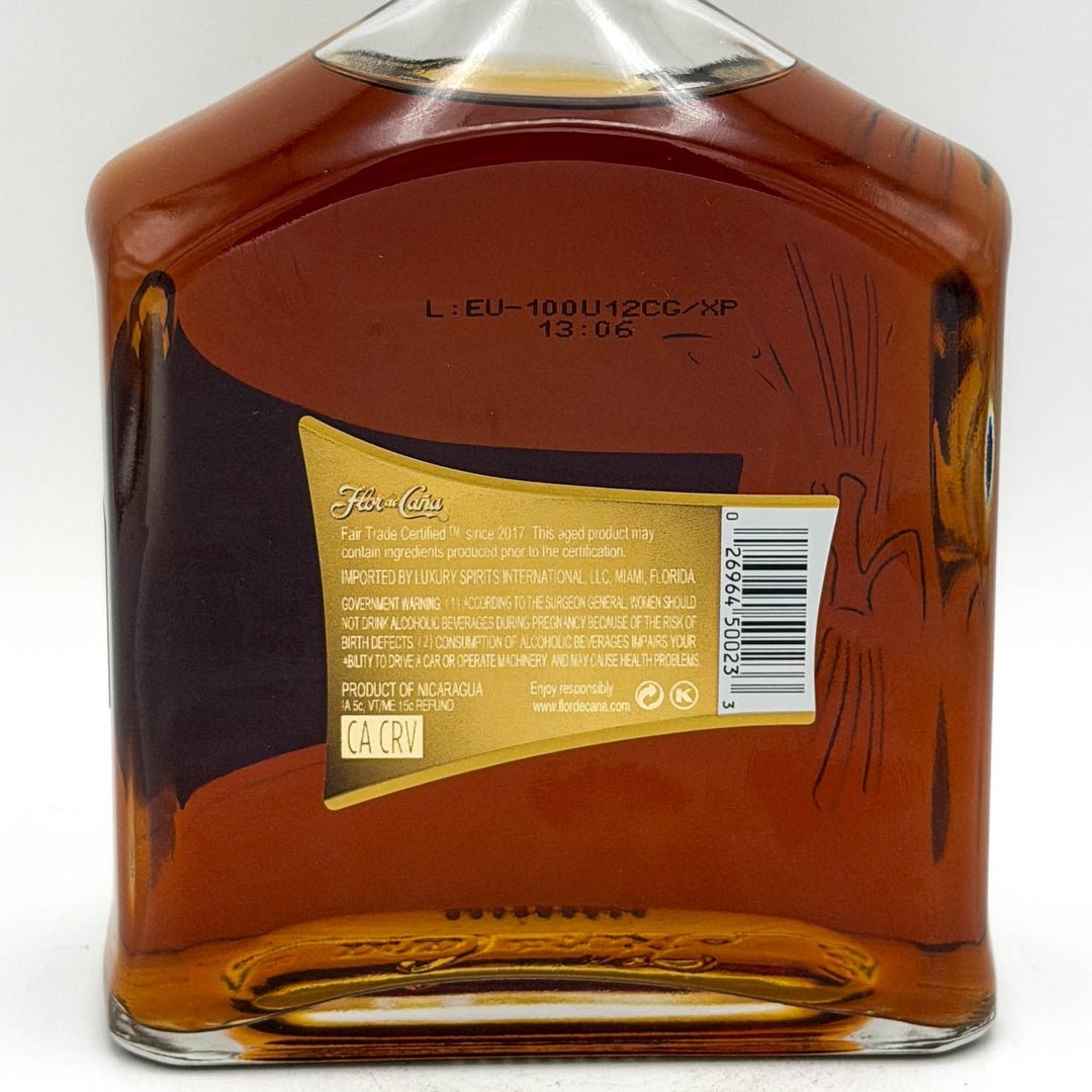 Back view of a liquor bottle showing the amber liquid, printed text, and a gold product information label with a barcode on a white background.