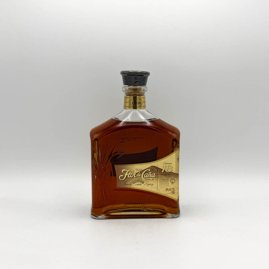 A close-up of a bottle of Flor de Cana 18 Years Old rum, showing the amber liquid and the cream and gold label with black and gold text.
