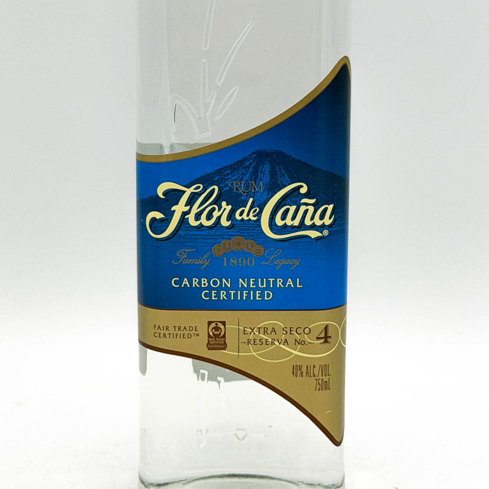 A clear glass bottle of Flor de Caña Carbon Neutral Certified tequila with a blue and gold label, shown against a plain white background.