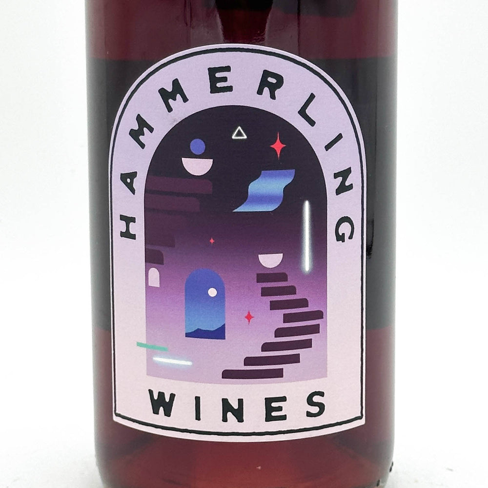 Close-up of a dark glass wine bottle with a large arched label reading HAMMERLING WINES. The label features a stylized purple and blue architectural illustration with geometric shapes on a white background.
