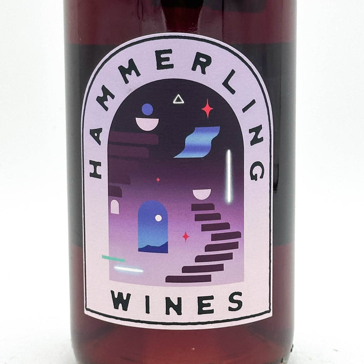 Close-up of a dark glass wine bottle with a large arched label reading HAMMERLING WINES. The label features a stylized purple and blue architectural illustration with geometric shapes on a white background.