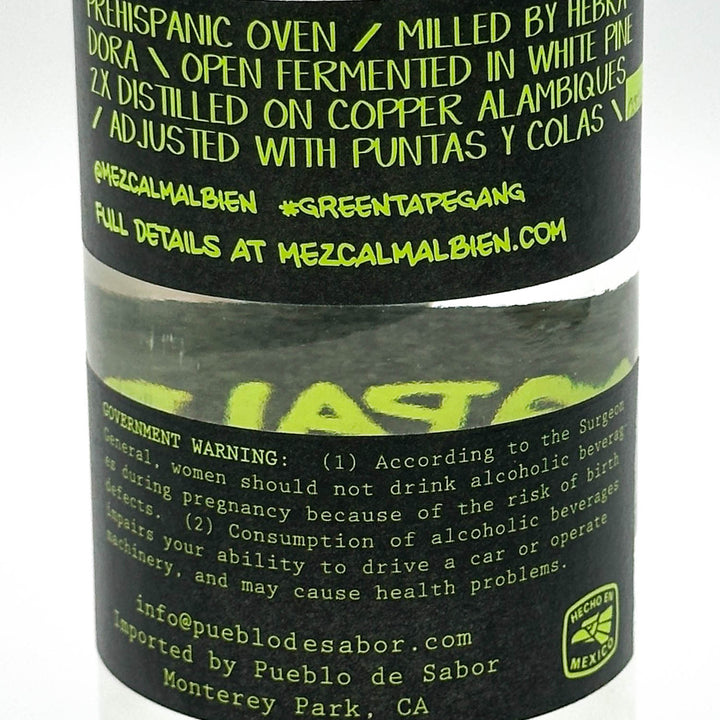 A close-up of a black cylindrical bottle label for Mezcal Malbien, featuring bright lime green text and a clear window showing the dark liquid inside. The label includes product details, ingredients, and a government warning.