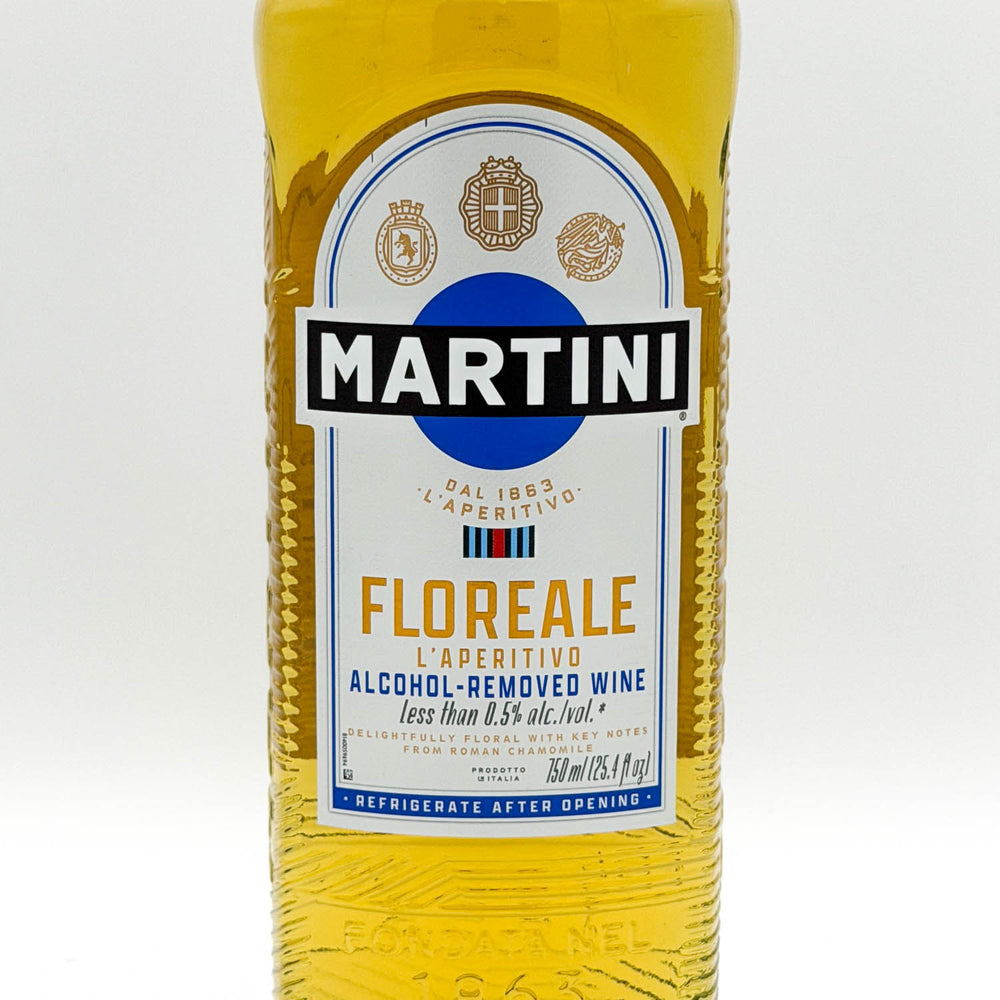 A bottle of Martini Floreale alcohol-free wine, showing the yellow liquid inside a textured clear bottle with a white, blue, and gold label.