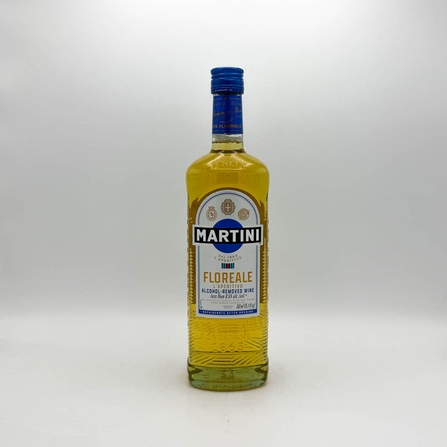 A bottle of Martini Florence non-alcoholic aperitif drink with golden yellow liquid inside, a blue cap, and a white and blue label, set against a plain light gray background.