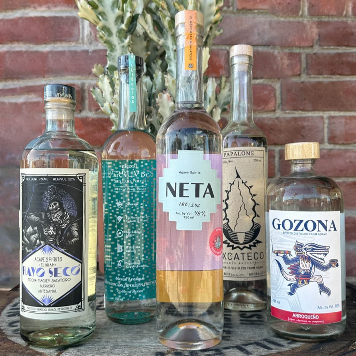 Five bottles of alcohol on a wooden tray with a brick wall background