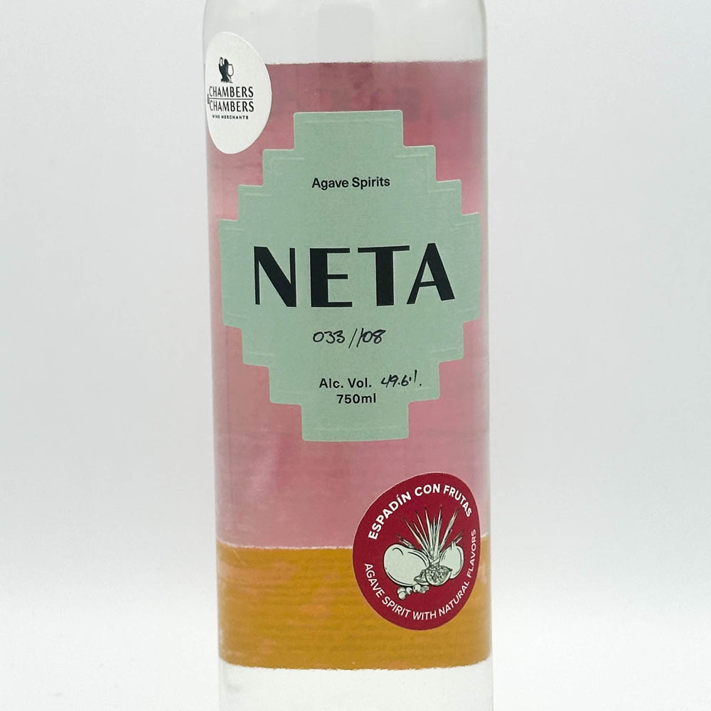 A bottle of Neta Agave Spirits with a pink and light green label, featuring a red circular sticker on the lower right, photographed against a plain white background.