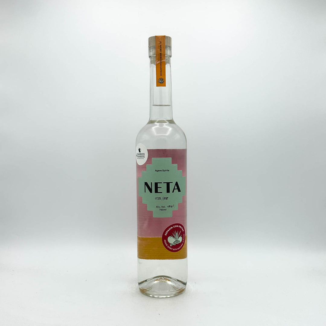 A clear glass bottle of Neta tequila with a pink and light green label, standing on a white surface against a light gray background.