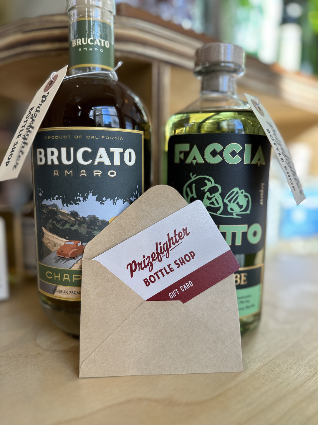 A gift card sticking out of a brown envelope in front of two different bottles of amaros