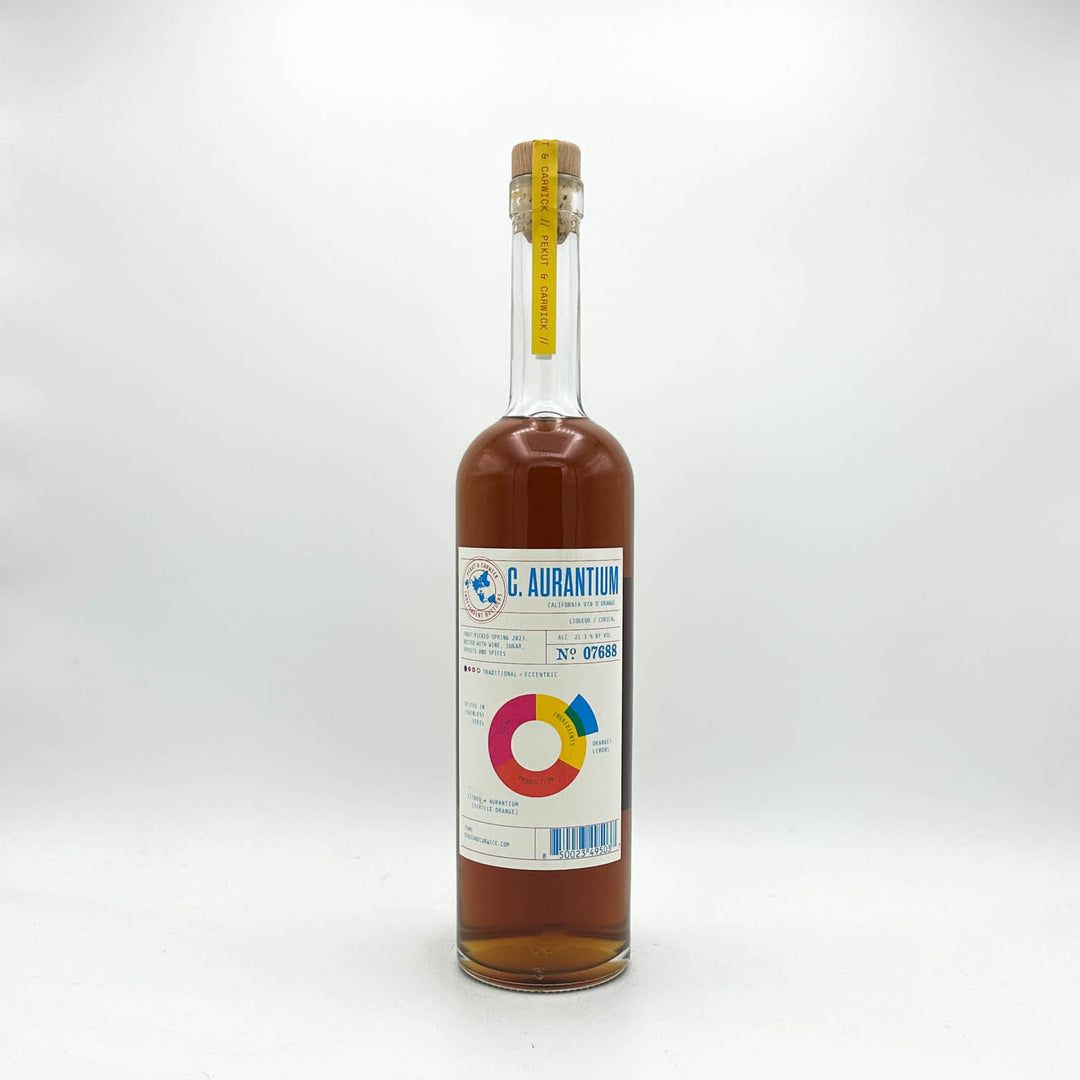 A clear glass bottle of C. Aurantium syrup with amber-brown liquid inside, a white label with blue and multicolor graphics, and a cork stopper with a yellow seal, photographed on a light gray background.