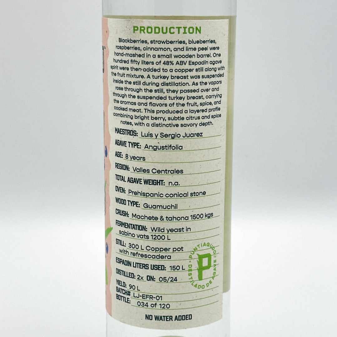 A close-up of the back of a tall cylindrical bottle with a cream-colored label, showing detailed production text and a green circular logo on a light gray background.