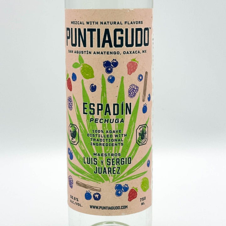 A bottle of Puntiagudo Espadín Pechuga mezcal with natural flavors, featuring a light peach label with illustrations of agave leaves and various berries, set against a clean white background.