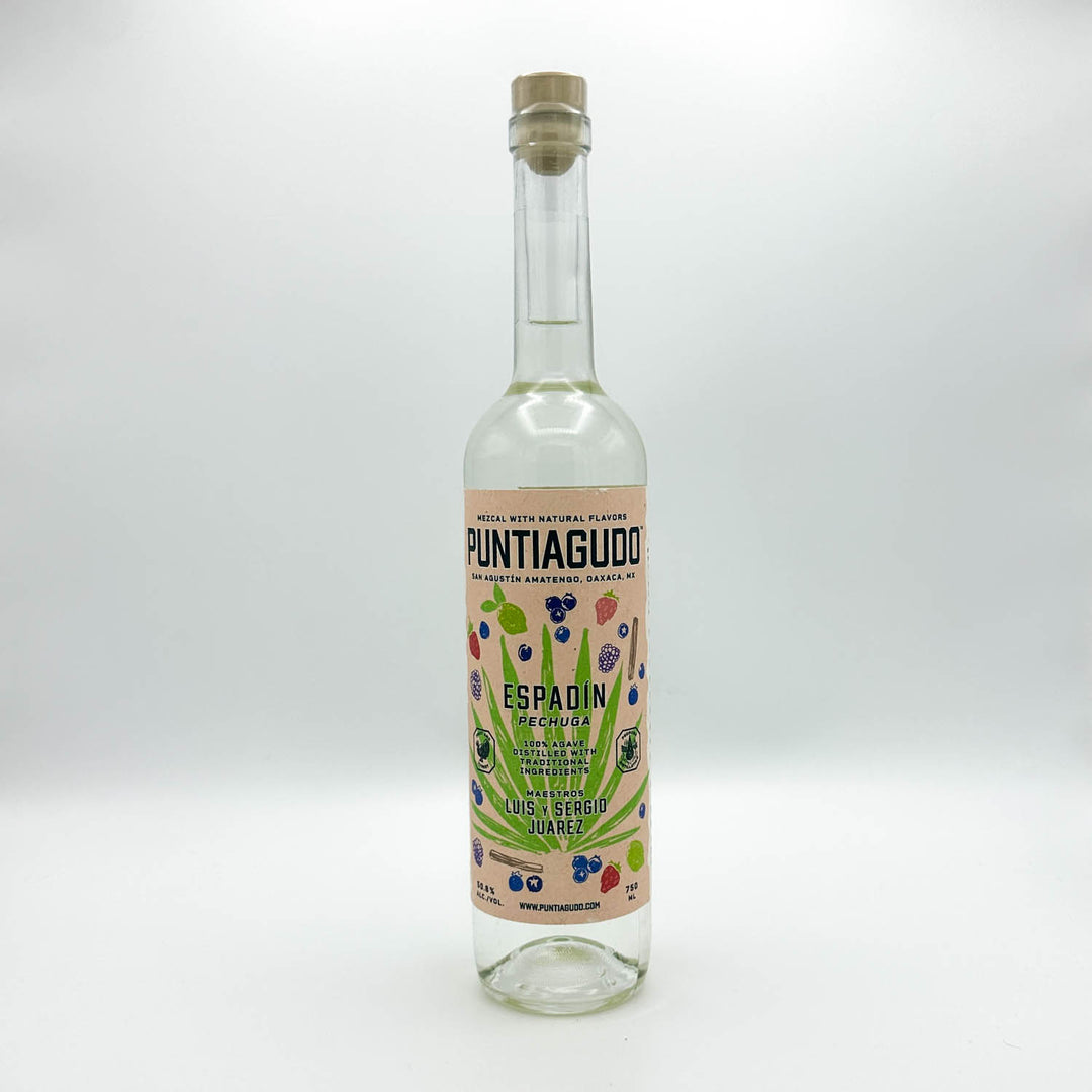 A clear glass bottle of Puntiguaddo Espadín (Spanish Blueberry Rum) with a cork stopper and a colorful label, photographed against a neutral light gray background.