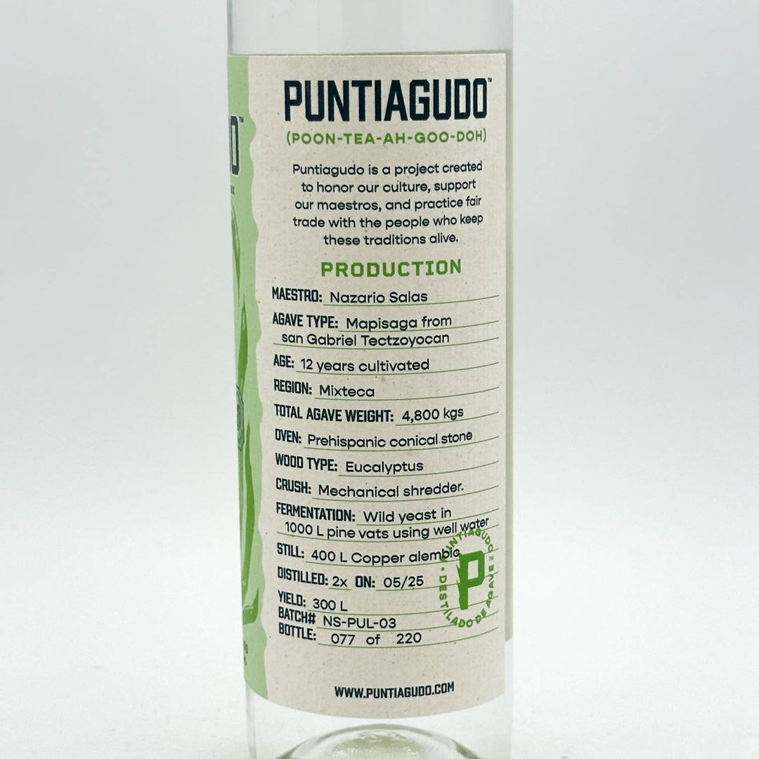 A clear glass bottle of Puntiagudo Poon-Tea-Ah-Goo-Doh tea, showing a white paper label with green and black text detailing production information.