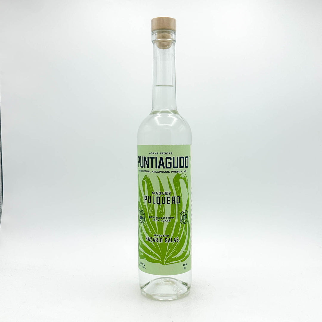 A clear glass bottle of Puntiguillo Made by Pulqueró tequila reposado, featuring a light green label with a green leaf design and a natural cork stopper, set against a plain white background.