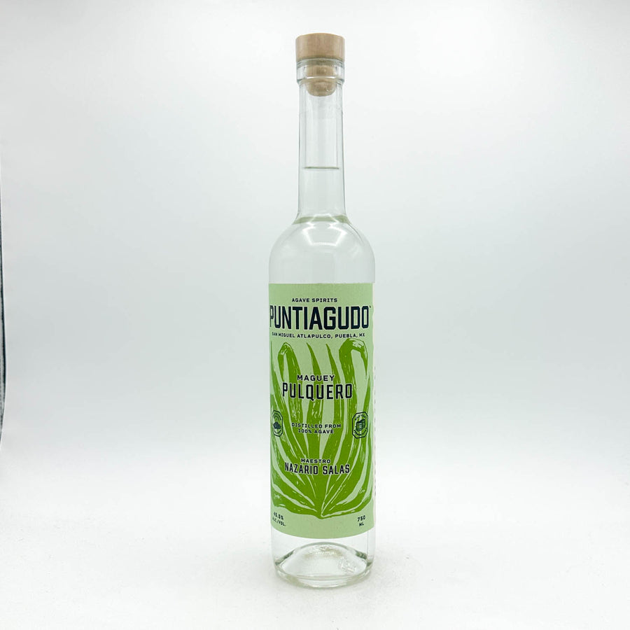 A clear glass bottle of Puntiguillo Made by Pulqueró tequila reposado, featuring a light green label with a green leaf design and a natural cork stopper, set against a plain white background.