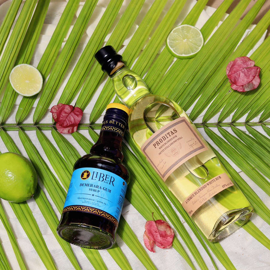 Two bottles of Liber and Prohibidas on a leafy background with limes and flowers.