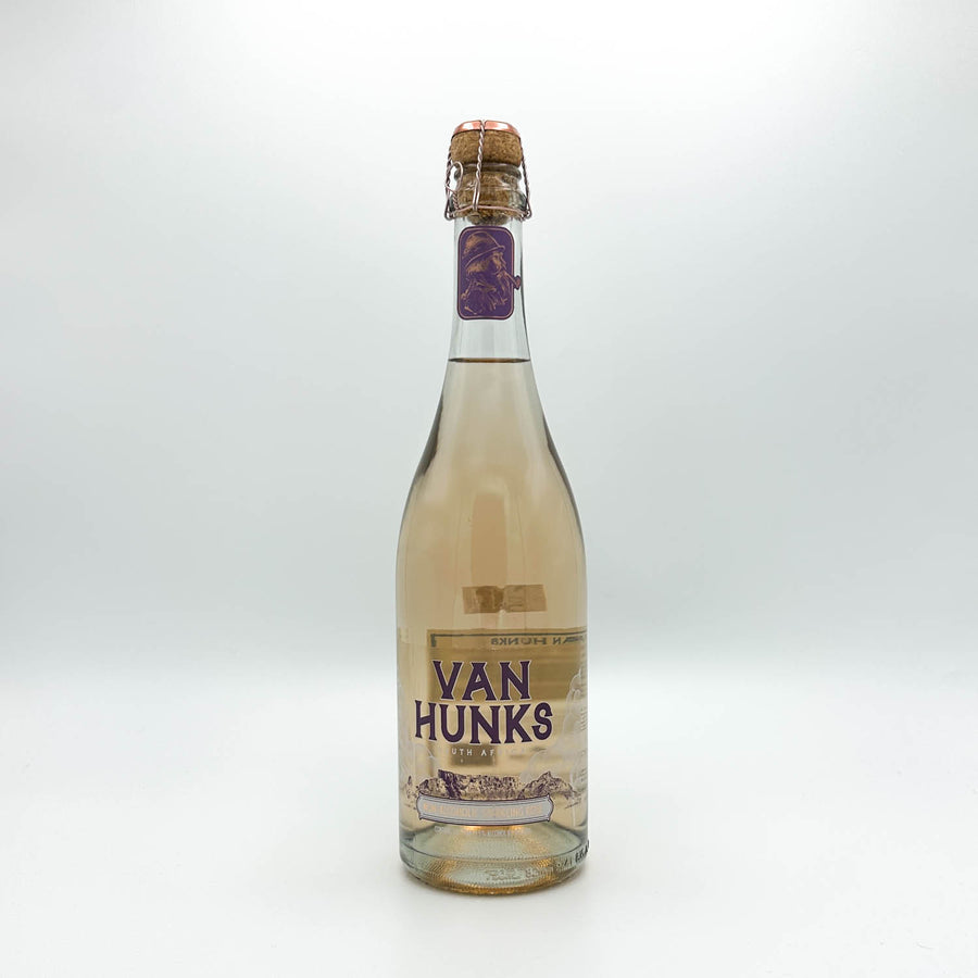 A bottle of Van Hunks sparkling wine with a light pinkish liquid, featuring a beige label with purple text and a cork closure, set against a plain light gray background.