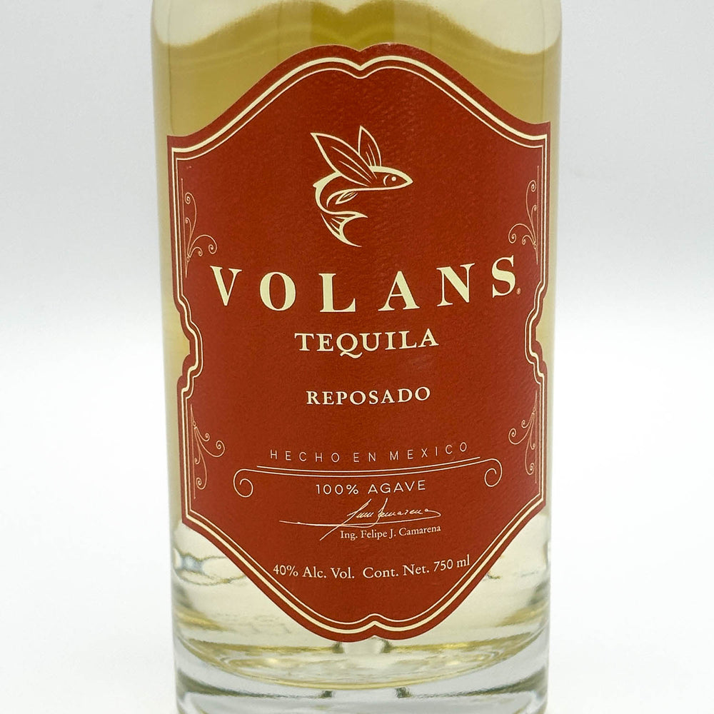 A bottle of Volans Tequila Reposado, showing the amber-brown liquid and a prominent reddish-brown label with gold lettering.
