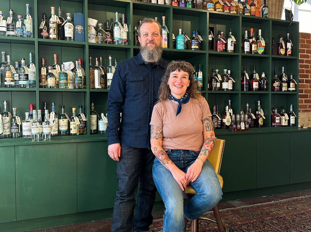 Owners Dylan and Polly in front of a shelf of spirits inside the shop
